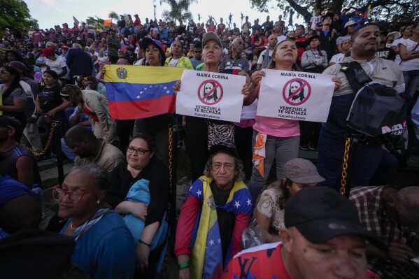 Supporters of President Nicolas Maduro hold Venezuelan flags and posters against opposition leader Maria Corina Machado during a Maduro speech in defense of his reelection, in Caracas, Venezuela, Tuesday, July 30, 2024. (AP Photo/Fernando Vergara)