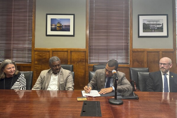 Montgomery Mayor Steven Reed signs a bill requiring photo ID for concealed firearm carry while city council member Julie Turner Beard, city council president Cornelius Calhoun, and police chief James Graboysat look on at Montgomery City Hall in Montgomery, Ala., on Sept. 6, 2024. (AP Photo/Safiyah Riddle/Report For America)