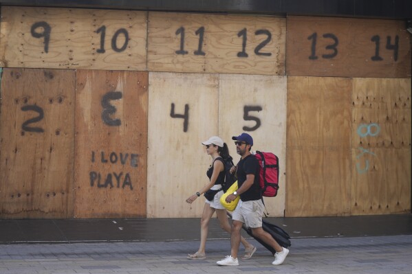 People walk past a souvenir shop's storefront boarded up preparation for the arrival of Hurricane Beryl, in Playa del Carmen, Mexico, July 4, 2024. (AP Photo/Fernando Llano)