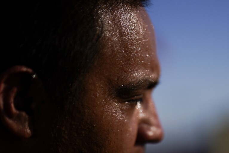 FILE - Juan Carlos Biseno sweats as he dances to music from his headphones as afternoon temperatures reach 115 degrees on July 19, 2023, in Calexico, Calif. The death certificates of more than 2,300 people who died in the United States last summer mention the effects of excessive heat, the highest number in 45 years of records, according to an Associated Press analysis of Centers for Disease Control and Prevention data. With May already breaking heat records, 2024 could be even deadlier. (AP Photo/Gregory Bull, File)