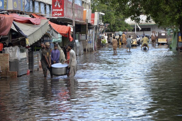 People wade through a flooded road caused by heavy monsoon rain, in Hyderabad, Pakistan, Friday, Aug. 30, 2024. (AP Photo/Pervez Masih)