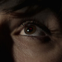 A red-eyed figure appears reflected in a woman's eyes.