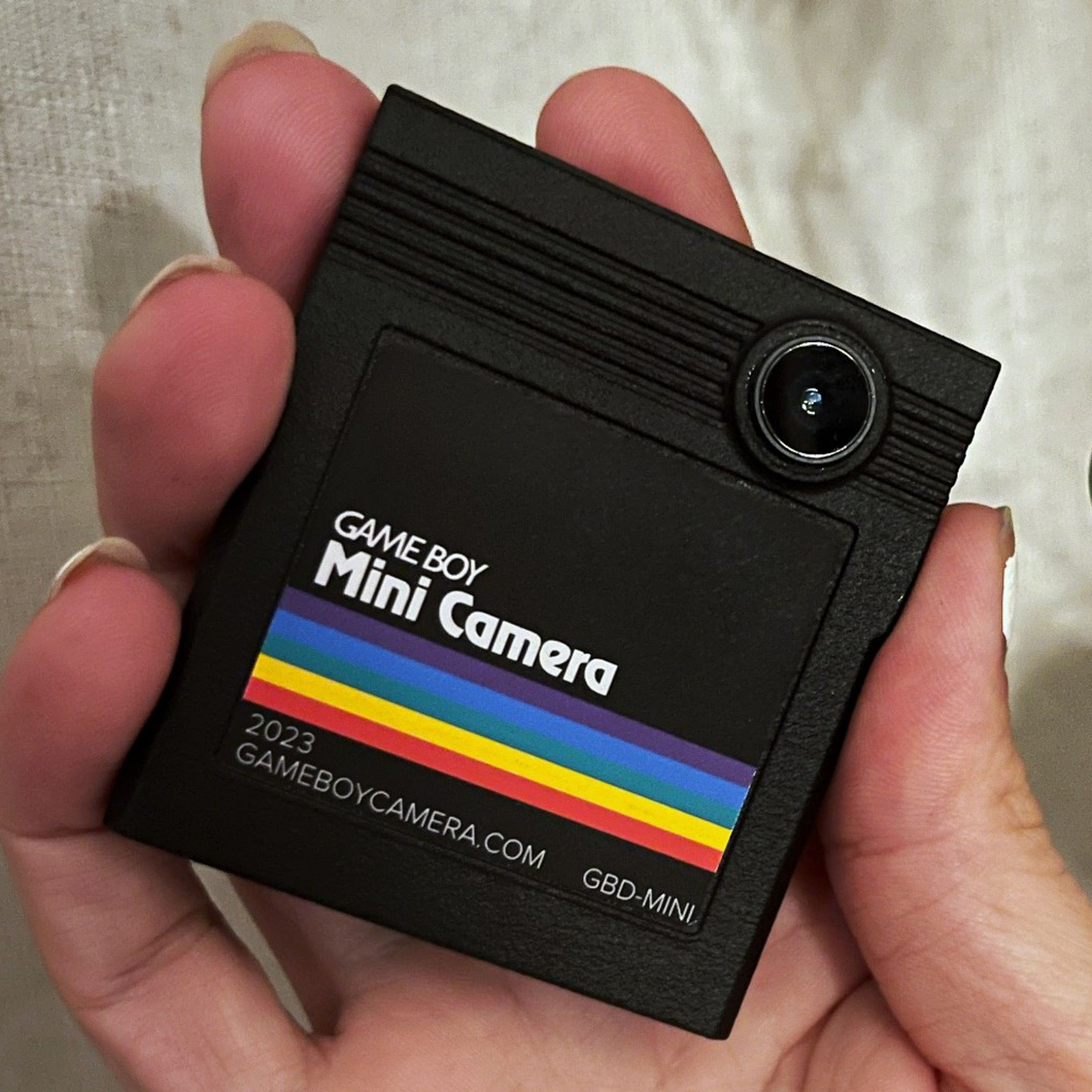 A black game boy cartridge with a rainbow stripe and an iphone lens sticking out.