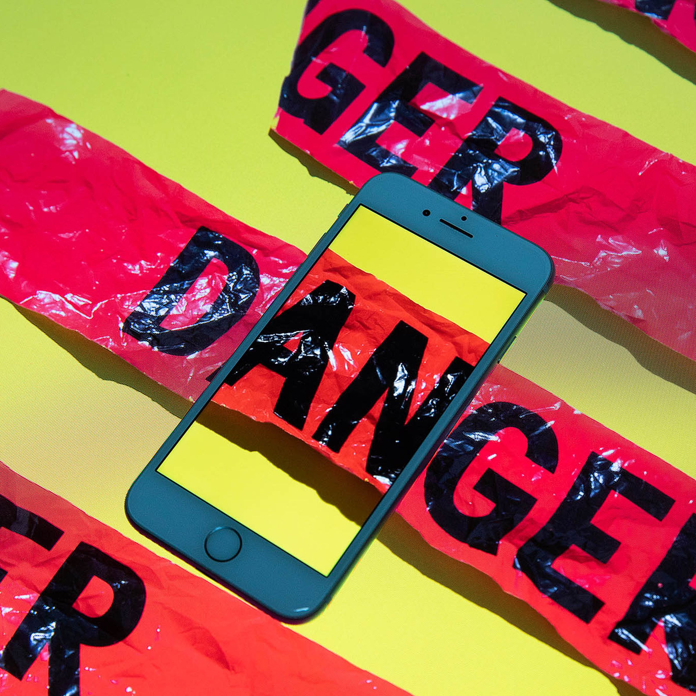 A smartphone sits on top of a surface with red tape reading “DANGER.” Where one strip intersects the phone, it continues inside the phone’s screen.