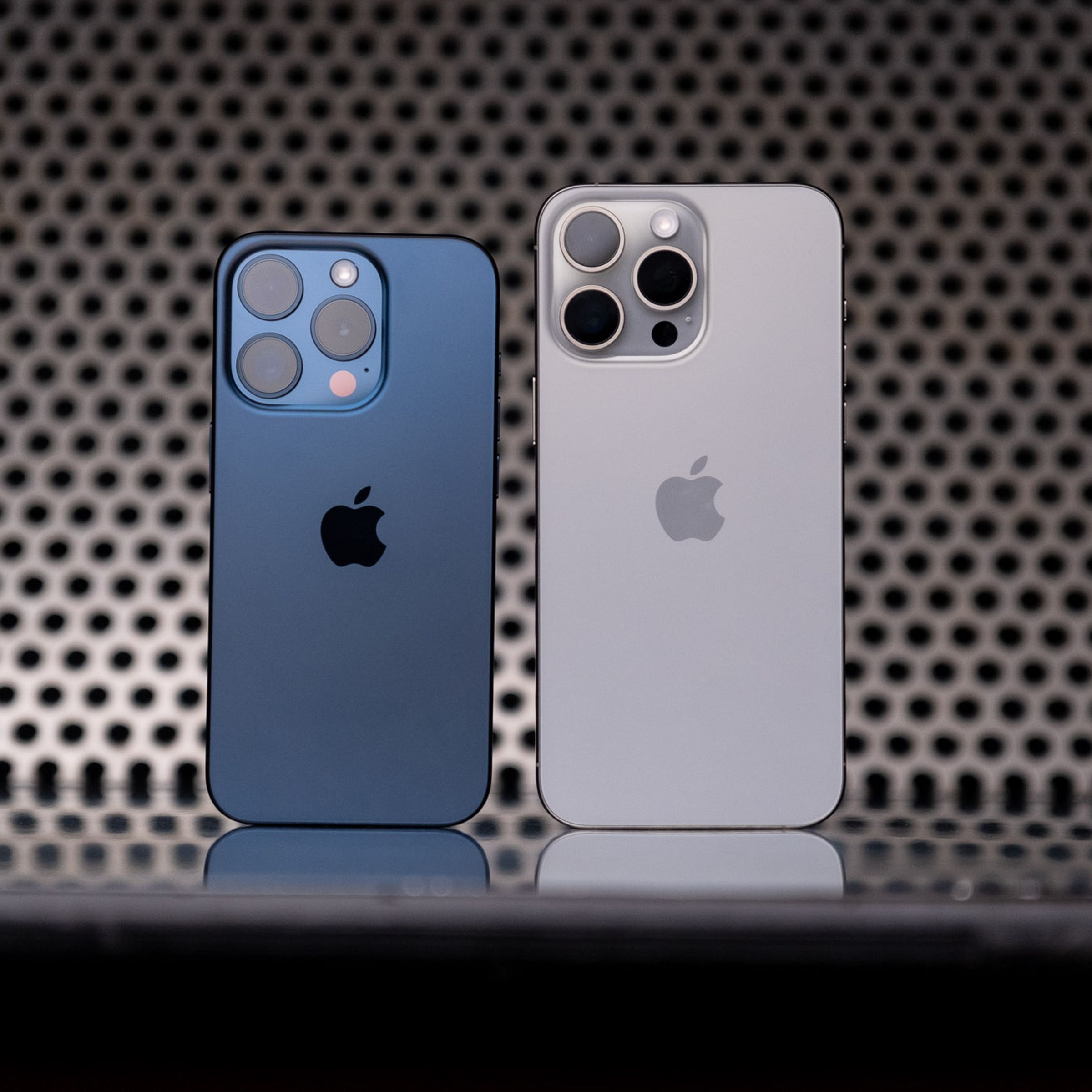 The iPhone 15 Pro (blue titanium) and 15 Pro Max (white titanium) standing next to one another.