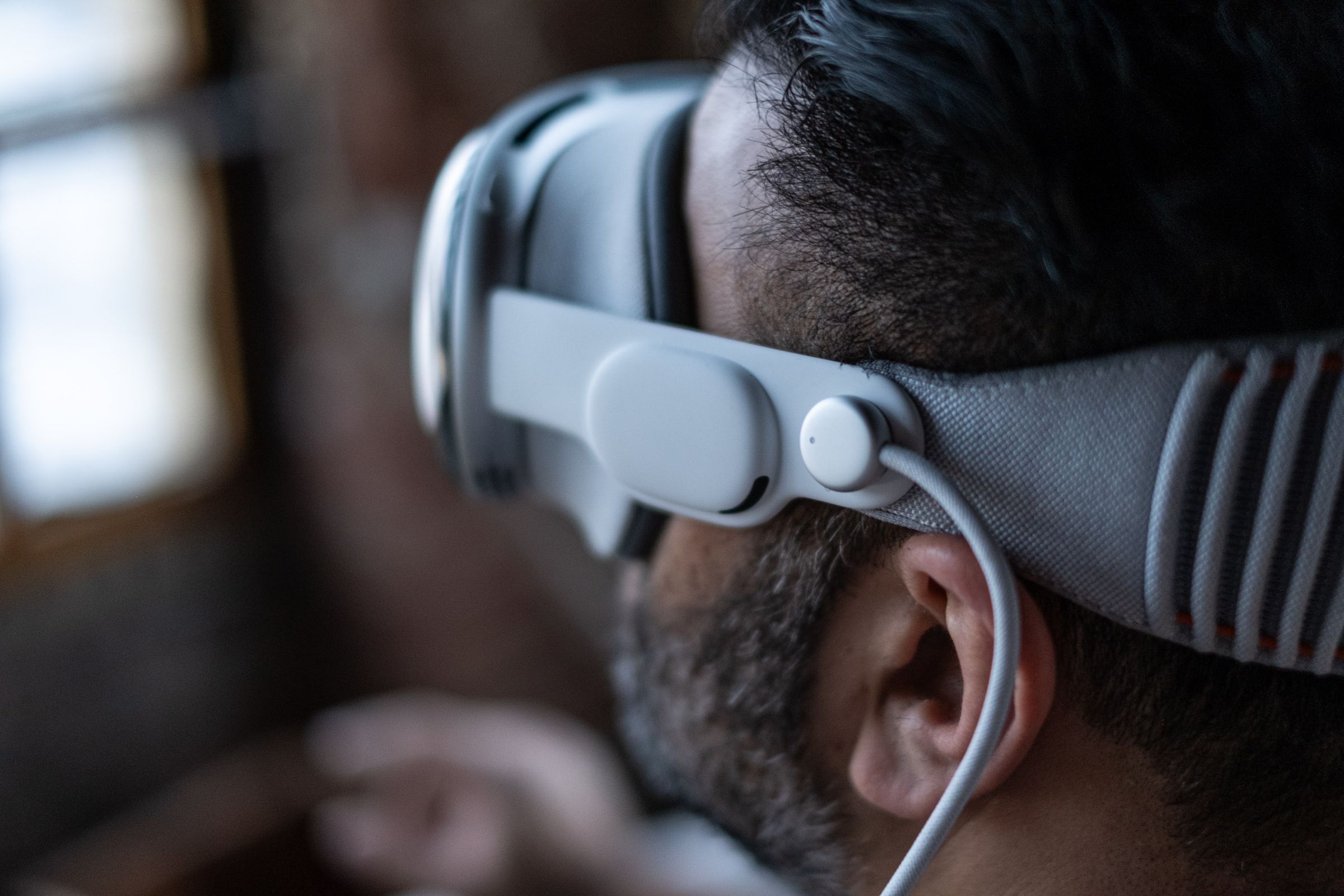 A man wears the Vision Pro headset, photographed from the side, showing off the power cable and the speaker.