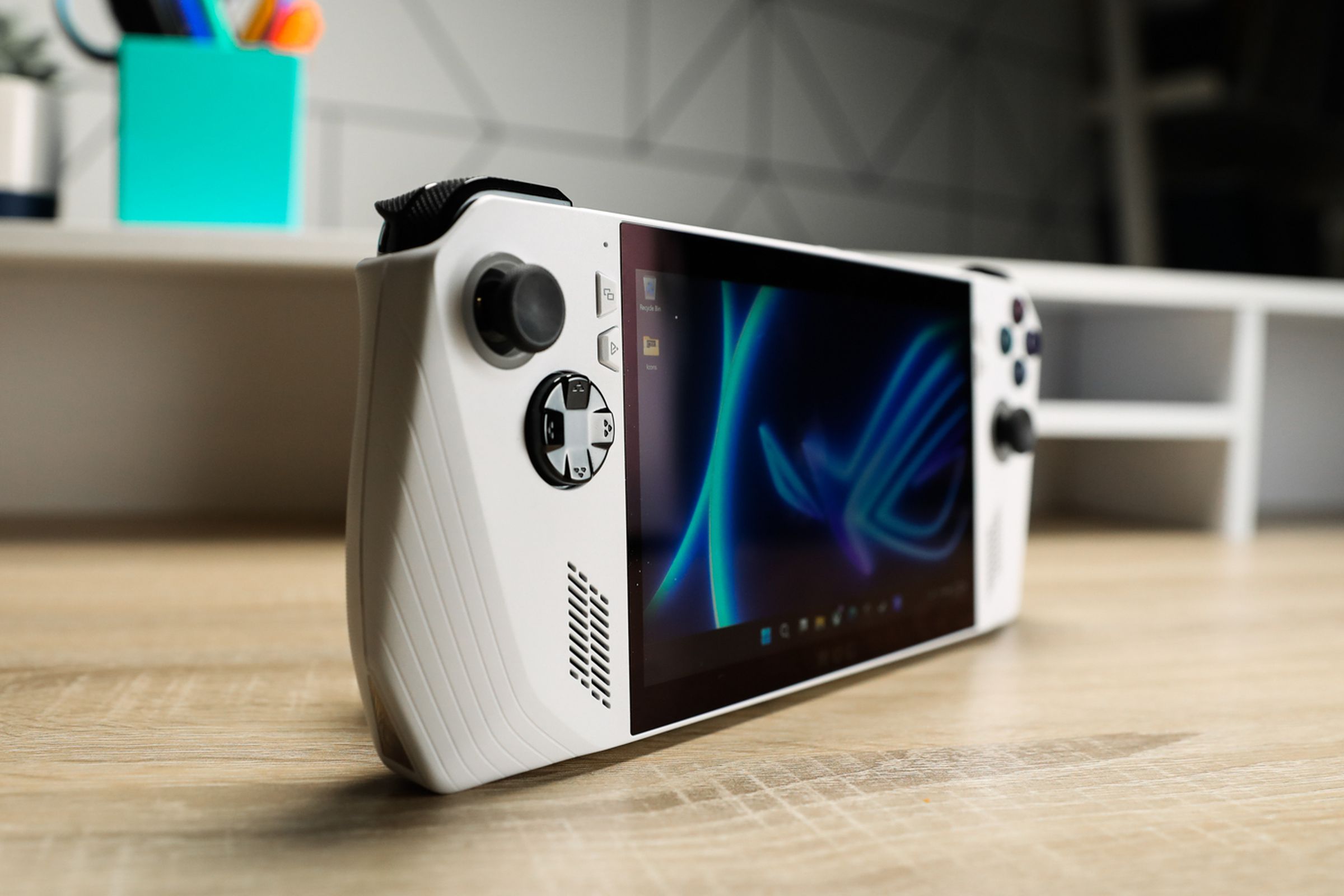 A white handheld with black joysticks and buttons sitting on a wooden desk with shallow depth of focus, at an angle to accentuate its profile.