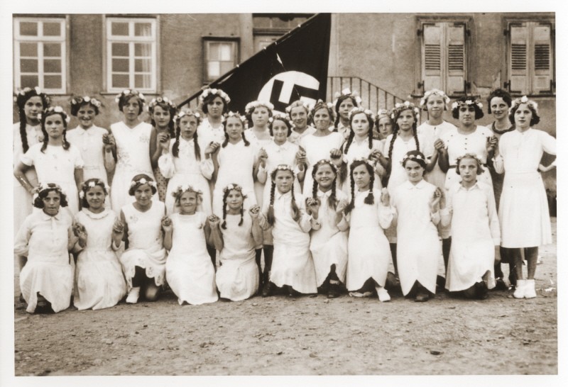 Group portrait of German girls posing outside their school in front of a Nazi flag.