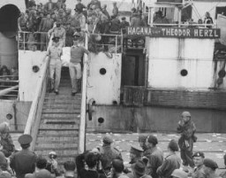 Palestine police remove the body of a refugee (draped in a Jewish flag), killed aboard the refugee ship Theodor Herzl during its unsuccessful attempt to run through a British naval blockade. Haifa port, Palestine, April 14, 1947.