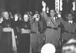 Le clergé catholique et les dignitaires nazis, parmi lesquels Joseph Goebbels (au bout à droite) et Wilhelm Frick (second à partir de la droite), font le salut nazi. Allemagne, date incertaine.