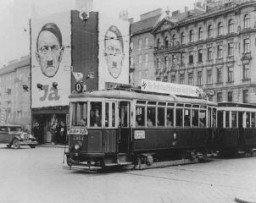 Üzerinde gamalı haçlar bulunan bir tramvay, Hitler’in resminin yer aldığı ilan panolarının önünden geçiyor. İlan panolarında Almanya’nın Avusturya’yı ilhak etmesine ilişkin referandumda Avusturyalılardan “Evet” (Ja) oyu vermeleri isteniyor. Viyana, Avusturya Nisan 1938.