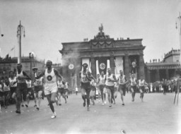 Pada 1 Agustus 1936, Hitler membuka Pertandingan Olimpiade Musim Panas ke-11. Sebagai pembuka ritual Olimpiade yang baru, seorang pelari tiba sambil membawa sebuah obor yang dibawa secara estafet dari lokasi Pertandingan kuno di Olympia, Yunani. Foto ini memperlihatkan pembawa obor Olimpiade yang berlari melintasi Berlin, melewati Gerbang Brandenburg, tidak lama sebelum upacara pembukaan. Berlin, Jerman, Juli-Agustus 1936.