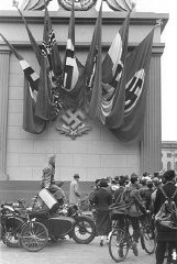 Berlin’de Nazi bayrakları ve gamalı haçla süslenmiş anıtın yanında bulunan Nazi toplanma yerindeki Alman izleyicileri. Almanya, 1937.