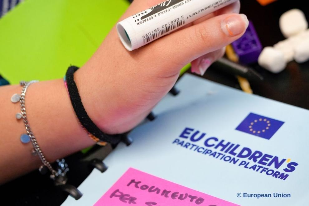 A child's hand holding a black marker, together with a post it sticker on a notebook