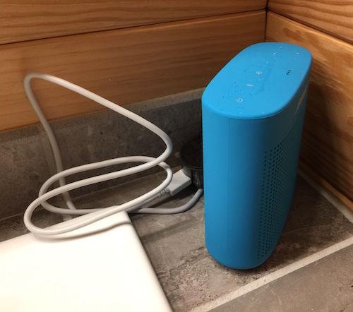 A teal-blue bluetooth speaker sitting on a counter in a bathroom