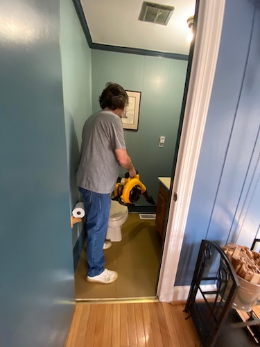 A man in a blue shirt holding a yellow and black Dewalt battery powered leaf blower in a blue half bath off of a kitchen