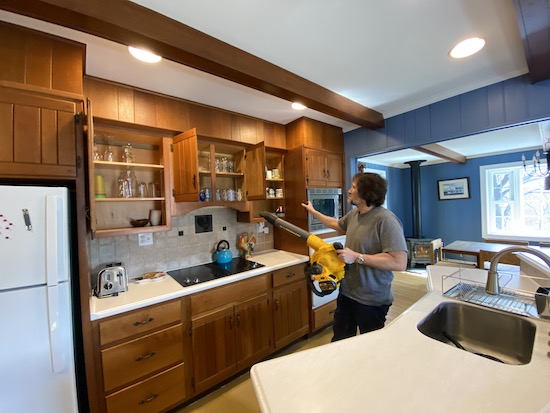 A man holding a yellow and black Dewalt battery powered leaf blower up to a kitchen cabinet full of glasses and dishes