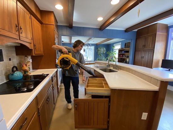 A man in a blue shirt holding a yellow and black Dewalt battery powered leaf blower under a kitchen sink