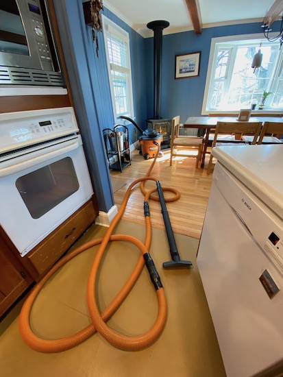 An orange and black shop vacuum with it's black exhaust tube out a window in a blue kitchen