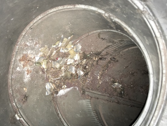 Looking into a metal duct at a pile of dirt mixed with yellow pieces of fiberglass and tin foil paper which was the backing to the fiberglass.