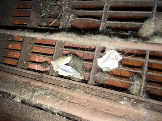 A copper colored air grate with fiberglass and paper intertwined into the slats