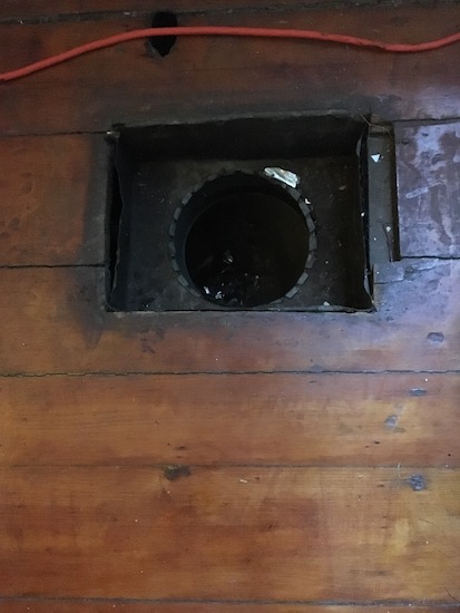 Looking down at a hole in a hardwood floor that has the air duct grate taken off showing the metal ductwork.