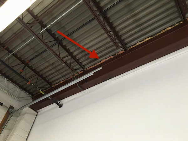 An arrow pointing to fiberglass insulation along a beam in an industrial building