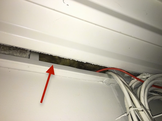 An arrow pointing to fiberglass insulation along the ceiling of an industrial building where the wires go into the wall