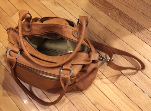 A honey brown leather purse tote bag with a tan microfiber interior sitting on a hardwood floor