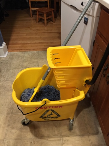 A yellow industrial size mop and bucket in a kitchen of a house