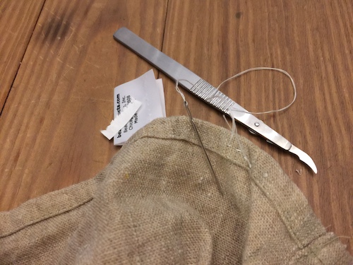 A seam stripper and a needle next to a tag that was just cut off of a hemp shower curtain