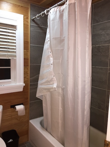 A white polyester shower curtain hanging in a bathroom over a white metal tub