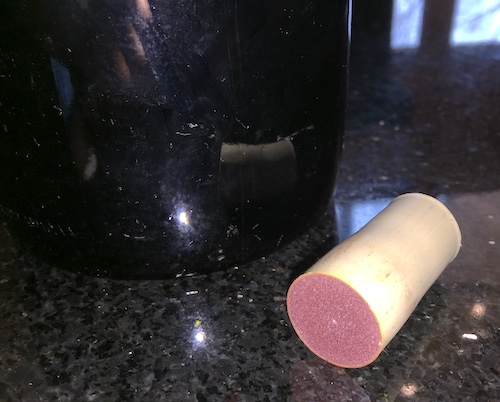 A tan synthetic cork with red wine staining it on a black countertop