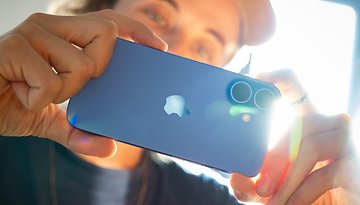 A person holding an Apple iPhone 16, showcasing its blue color and dual camera setup.