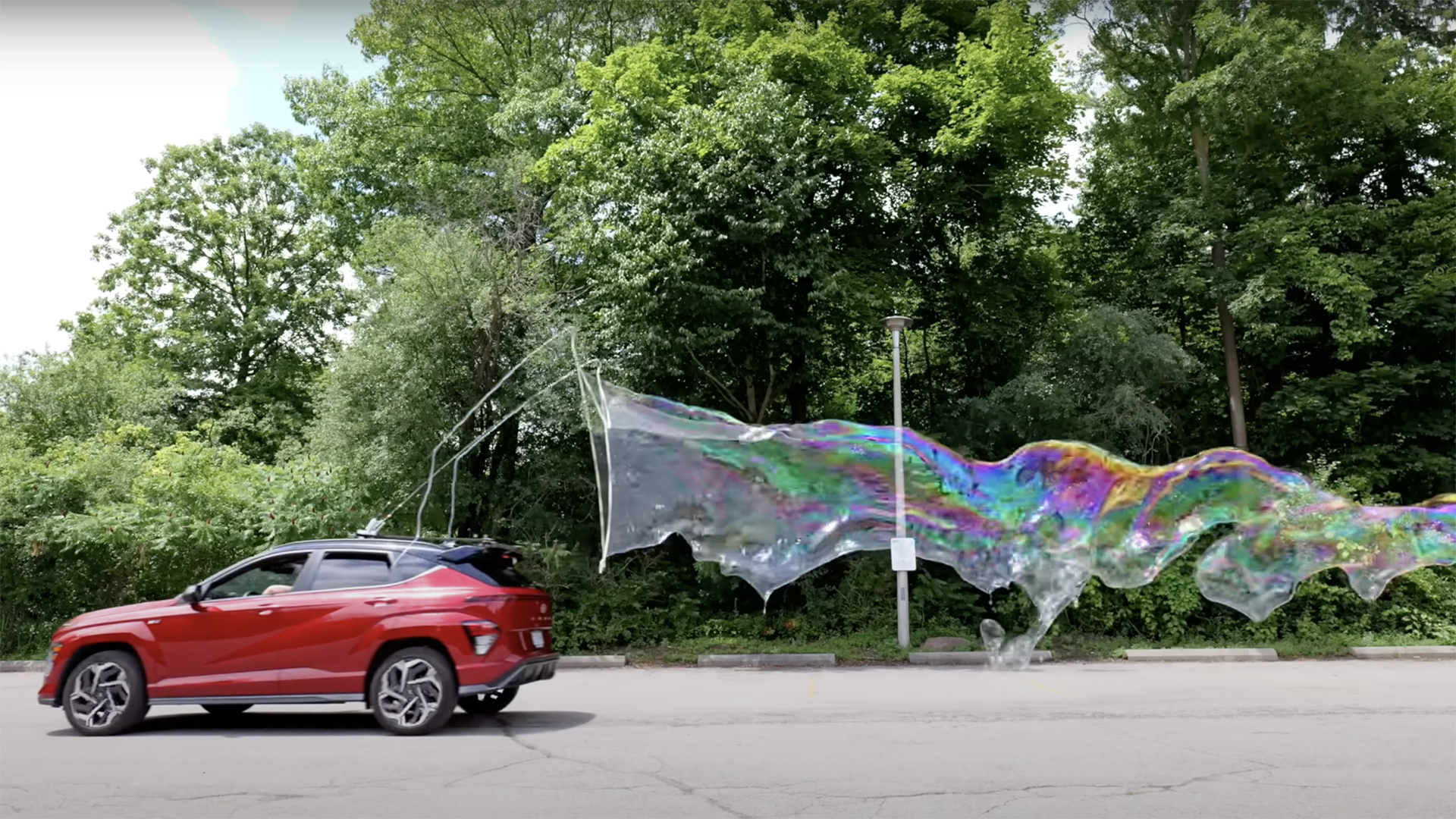 A red car with a DIY bubble making machine mounted on top creating a large bubble