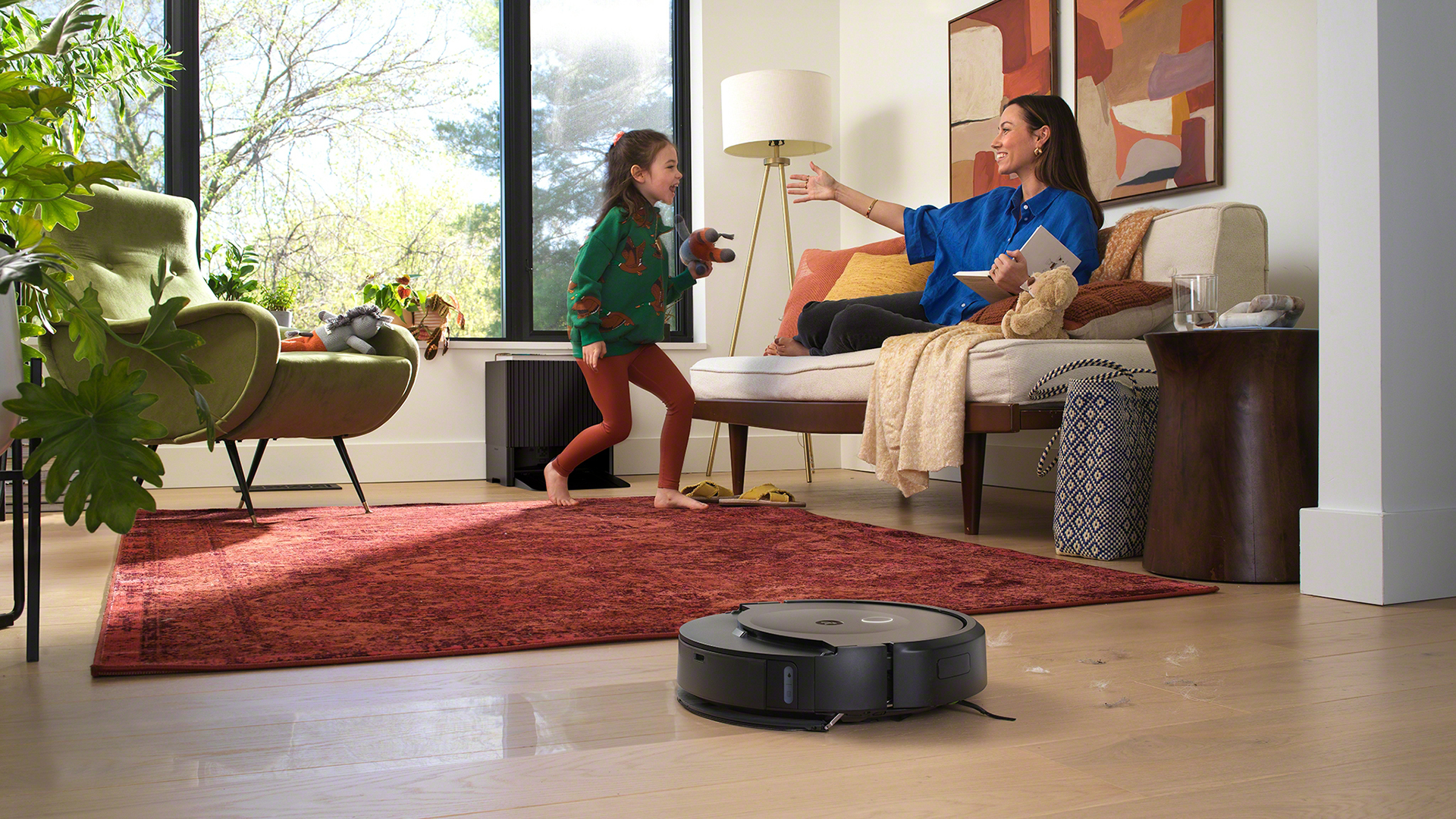 Lifestyle shot of Roomba Combo 10 Max cleaning floor with woman and child in the background.