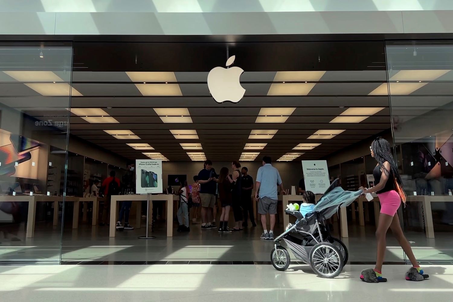 A woman pushing a stroller walks past an Apple store.