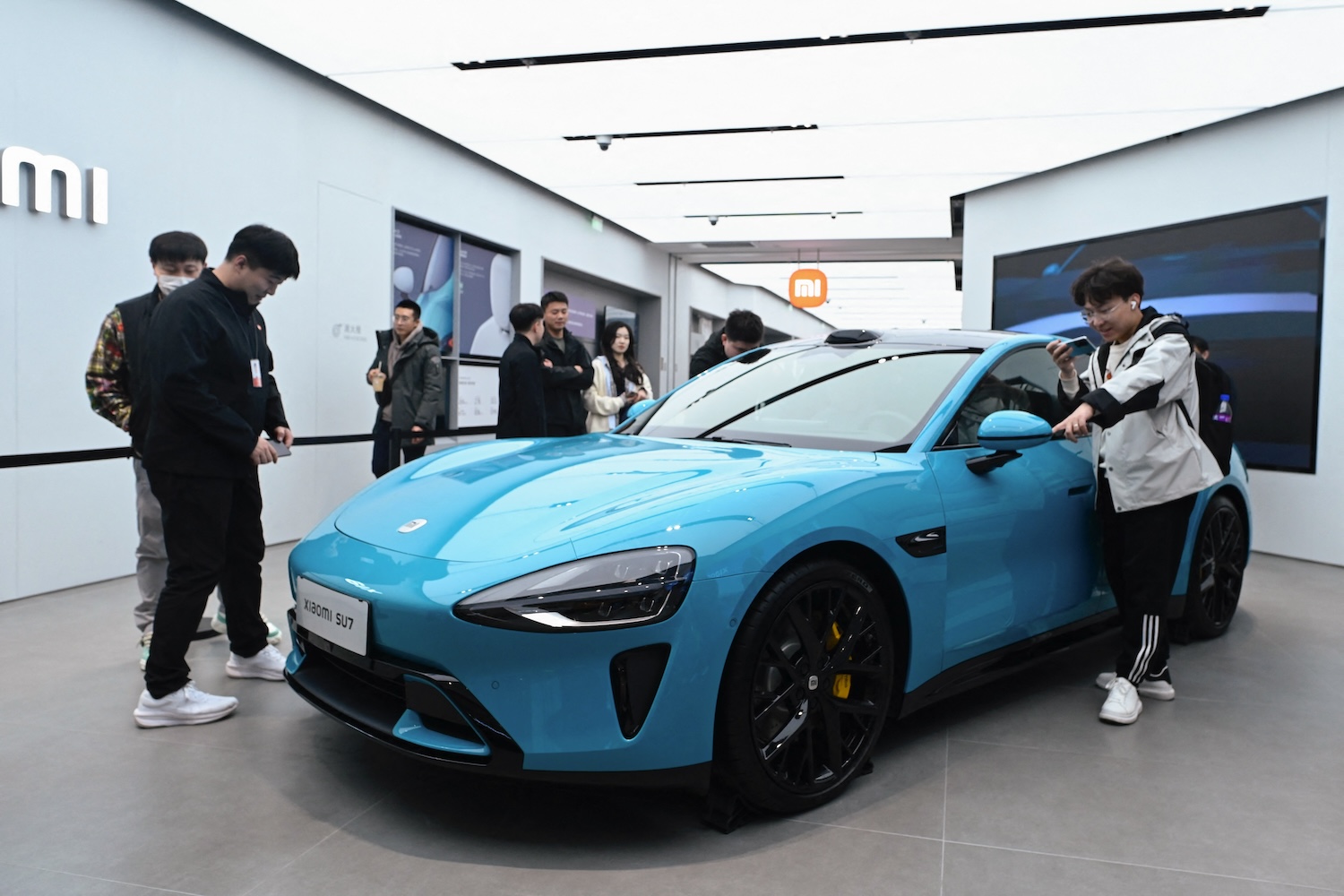 Xiaomi's SU7 electric car displayed in a showroom, with individuals standing around it taking pictures.