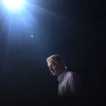 Geoffrey Hinton speaks at an event with a spotlight shining on him against a dark background.