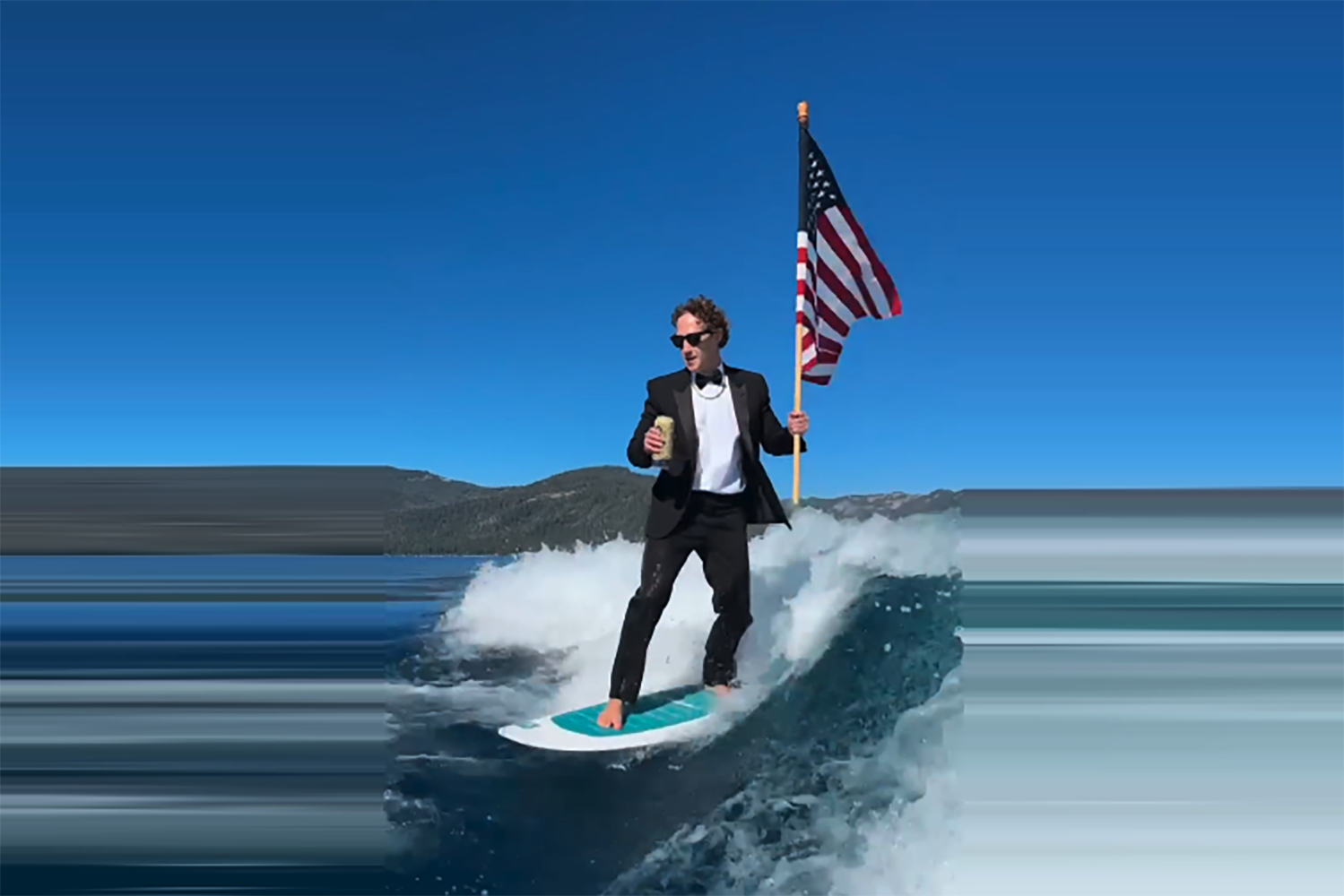 Zuckerberg surfs while waving and American flag and drinking a beer.