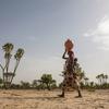 A woman carries a baby and a water container as she walks across arid land in Niger.