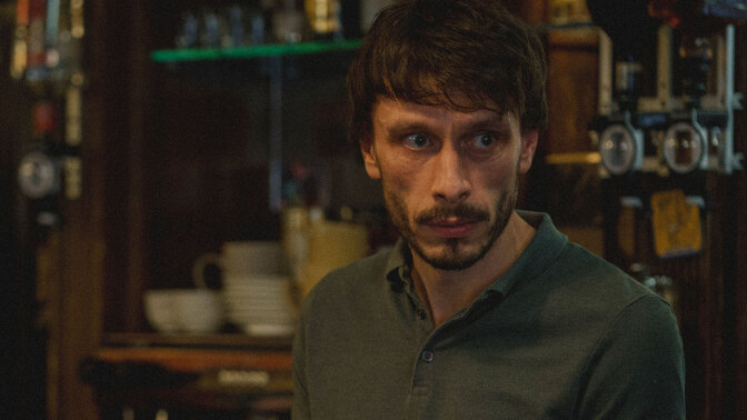 A man stands behind the bar in a pub.