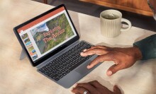 a person uses the amazon fire max 11 tablet with a keyboard while sitting at a table. a white mug of tea sits off to the right of the tablet with keyboard