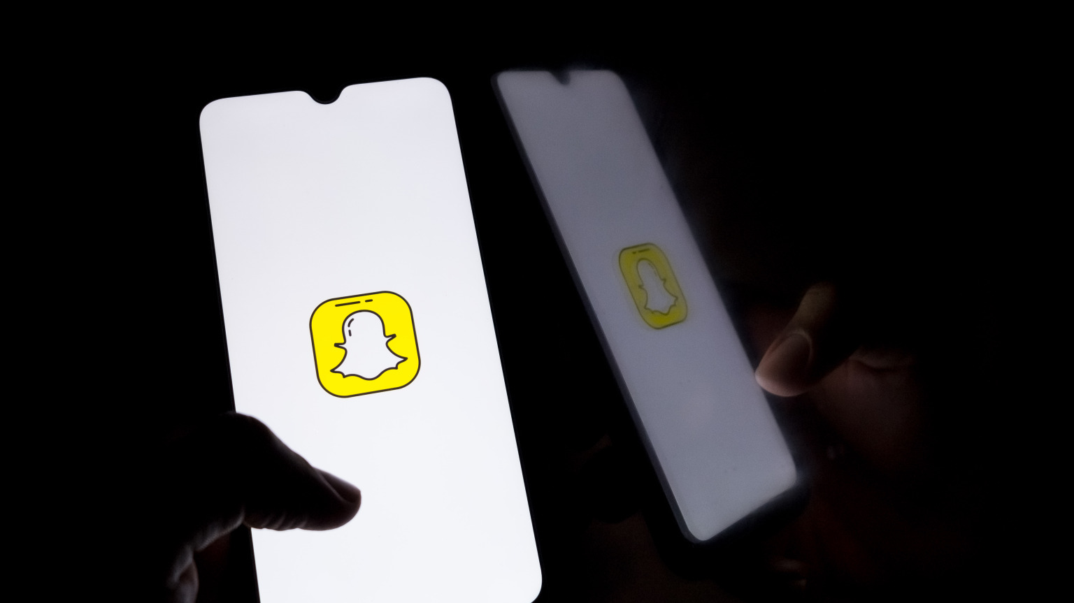 A hand holds a glowing phone showing the Snapchat logo in a dark room.