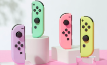 the pastel nintendo switch joy-cons upright on white and clear stands against a pink backdrop