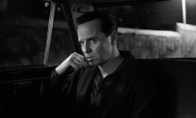 A man sits in a dark taxi looking intense.