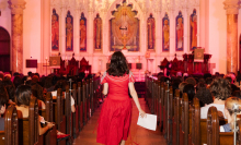 Rayne Fisher-Quann walking down the aisle of a church in a red dress. 
