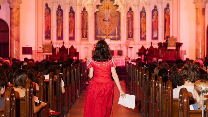 Rayne Fisher-Quann walking down the aisle of a church in a red dress. 
