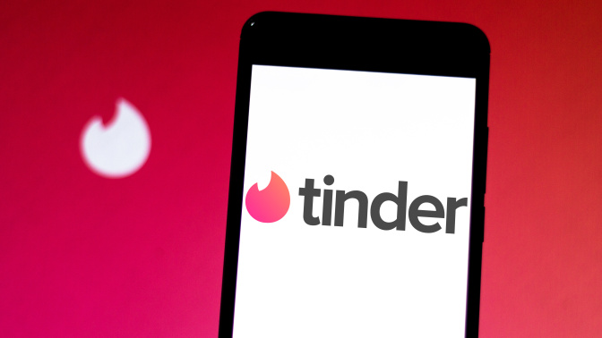 tinder logo on iphone in front of backdrop of tinder fire emblem