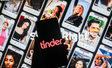 phone with black and pink tinder logo in front of backdrop of various tinder profiles